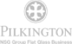 The Pilkington Glass logo in grey, featuring a circular emblem with a cross above the text "PILKINGTON." Below the brand name, there is a tagline that reads "First in Glass." The logo represents the company's expertise and heritage in glass manufacturing.